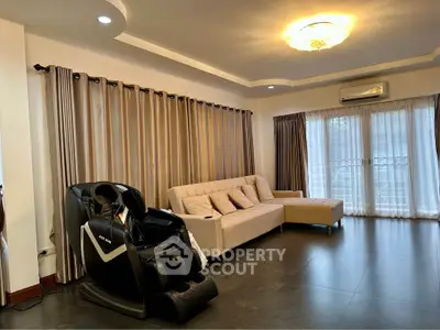 Spacious living room with modern massage chair and elegant sofa, featuring large windows and stylish curtains.