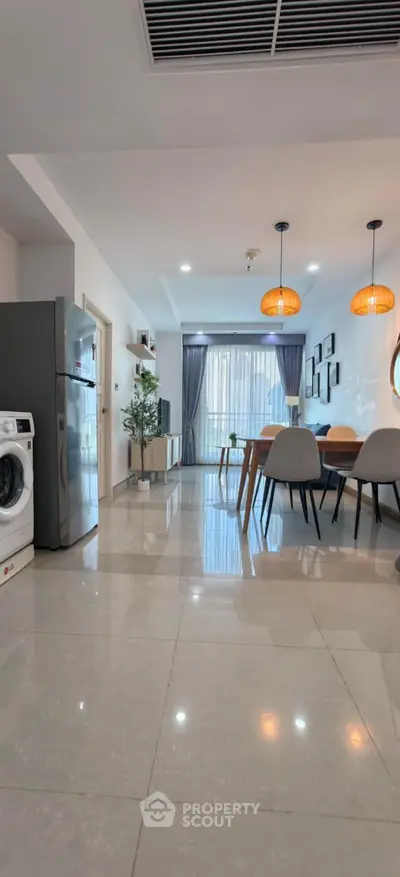Modern open-plan living room with dining area, featuring stylish lighting and sleek appliances.