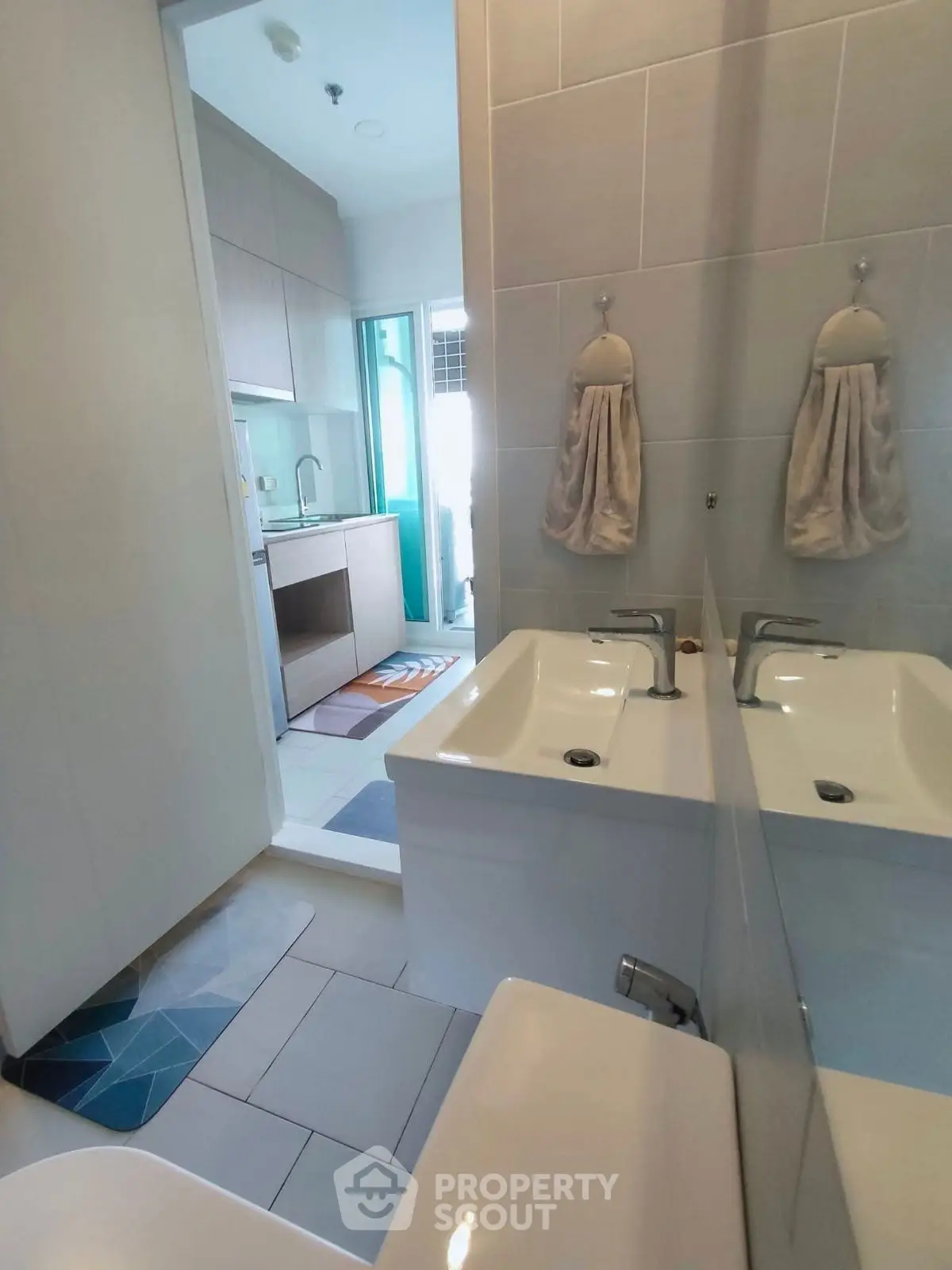 Modern bathroom with dual sinks and view into a sleek kitchen area.
