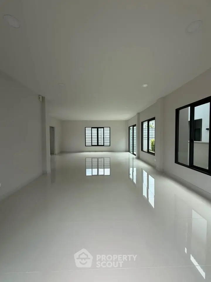 Spacious empty living room with large windows and glossy tiled floors in modern home.