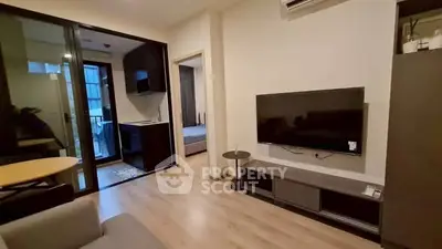 Modern living room with TV and open layout leading to kitchen and bedroom, featuring sleek design.