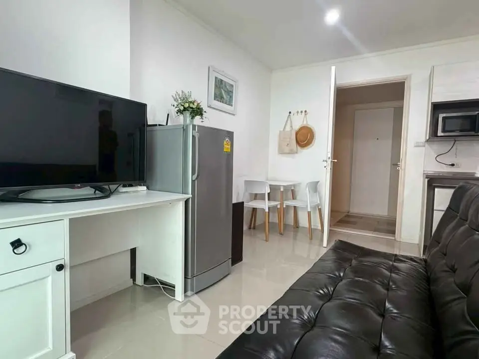Modern living room with sleek black sofa, flat-screen TV, and compact dining area in stylish apartment.