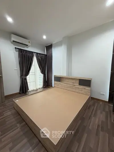 Spacious bedroom with modern wooden flooring and large window for natural light.