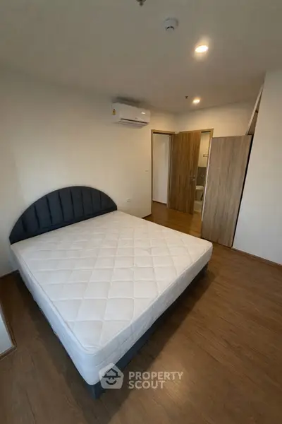 Spacious bedroom with modern design and wooden flooring, featuring a comfortable bed and ample natural light.