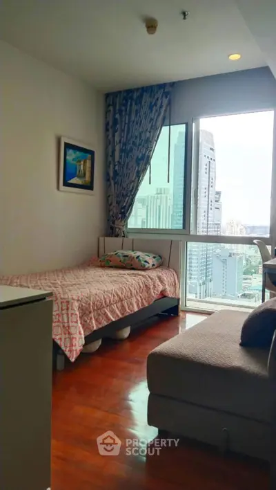 Cozy bedroom with city view in high-rise apartment, featuring wooden flooring and modern decor.