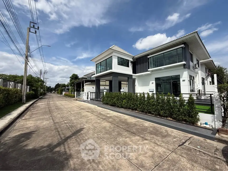 Modern two-story house with sleek design and lush greenery on a sunny day.