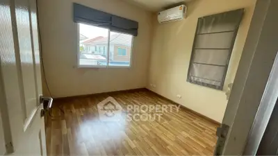 Spacious empty room with wooden flooring and large window, perfect for customization.