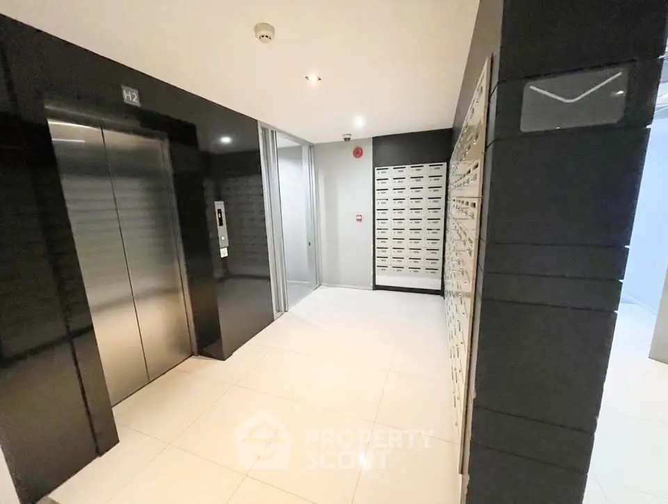 Modern building lobby with sleek elevator and mailboxes, featuring glossy tiles and contemporary design.