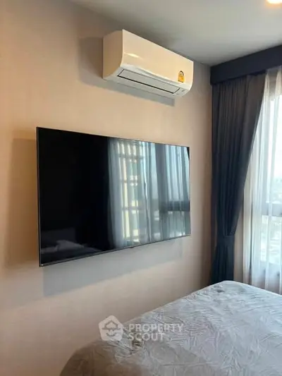 Modern bedroom with wall-mounted TV and air conditioning unit, featuring large window with curtains.