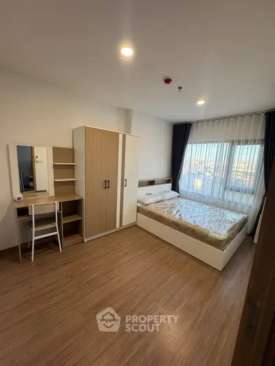 Modern bedroom with wooden flooring, large window, and stylish furniture in a cozy apartment.