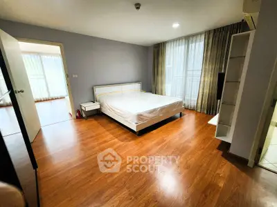 Spacious bedroom with wooden flooring and large windows for natural light.