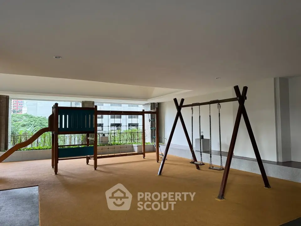 Spacious indoor playground with swings and slide in modern residential building.