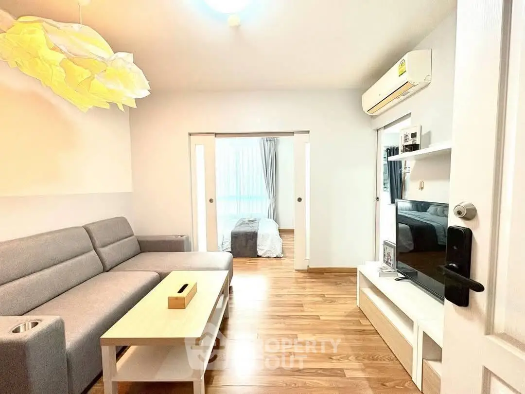 Modern living room with cozy sofa and TV, leading to a bright bedroom.