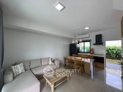 Modern open-layout living room with kitchen, featuring sleek furniture and natural light.