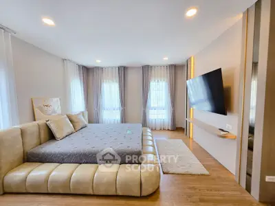 Luxurious modern bedroom with large bed and wall-mounted TV, featuring elegant decor and ample natural light.
