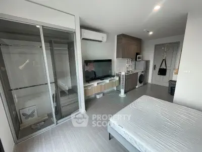 Modern studio apartment with sleek design, featuring a glass wardrobe, wall-mounted TV, and compact kitchen area.