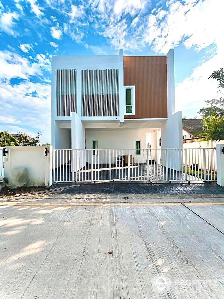 Modern two-story house with minimalist design and gated entrance under a clear blue sky.