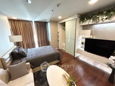 Modern bedroom with cozy decor and large TV, featuring elegant lighting and wooden flooring.