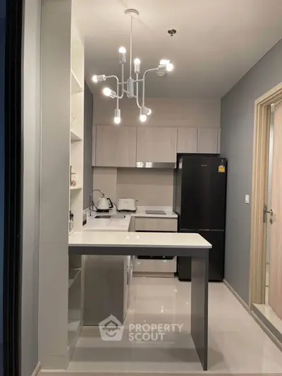 Modern kitchen with sleek design, featuring black fridge, washing machine, and elegant lighting.