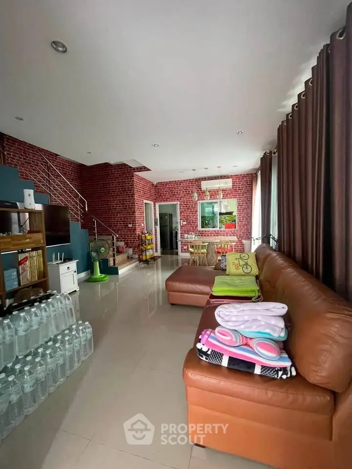 Spacious living room with modern decor and natural light, featuring a cozy leather sofa and stylish brick walls.