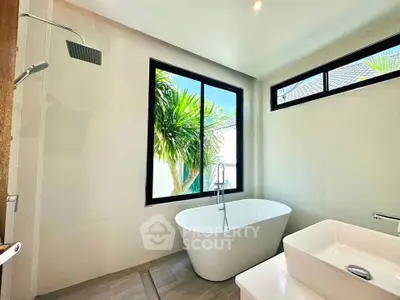 Luxurious bathroom with freestanding tub and tropical view, perfect for relaxation.