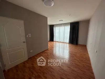 Spacious empty room with wooden flooring and large window, ideal for customization.