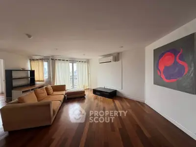 Spacious living room with modern art and natural light, featuring hardwood floors and a cozy sofa.