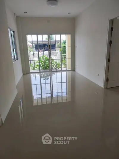 Spacious empty room with glossy floor and large windows offering natural light.