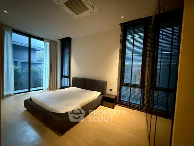 Spacious bedroom with large windows and modern design, featuring a minimalist bed and wooden flooring.