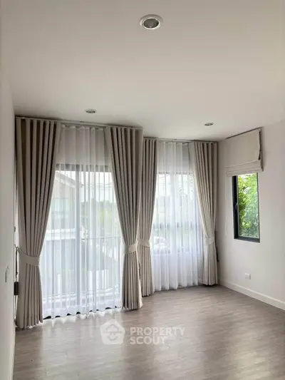 Spacious empty room with large windows and elegant curtains, perfect for natural light and modern living.