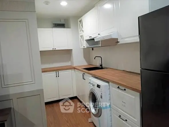 Modern kitchen with white cabinets, wooden countertops, and built-in washing machine.
