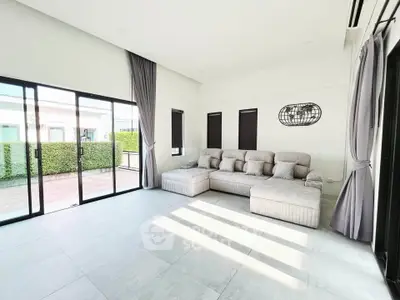 Spacious modern living room with large windows and stylish gray sofa, offering abundant natural light and garden view.
