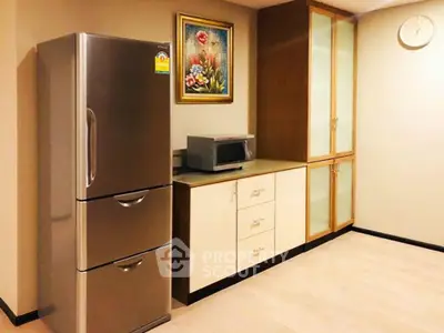 Modern kitchen with stainless steel fridge and microwave, featuring elegant cabinetry and a stylish painting.