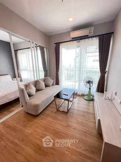 Modern living room with wooden flooring, cozy sofa, and large windows offering city views.