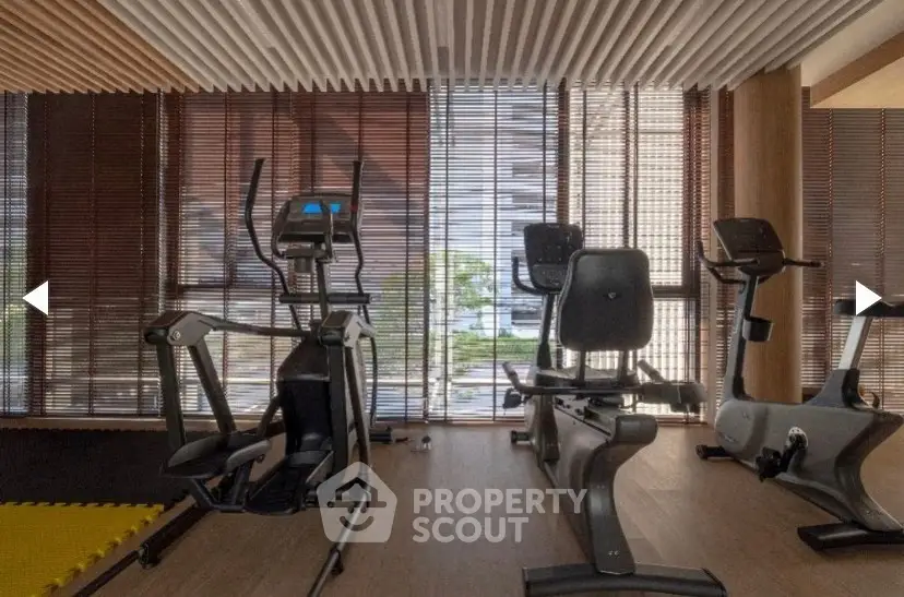 Modern gym with exercise equipment and wooden blinds in luxury building.