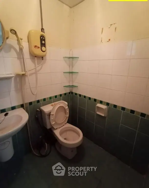 Compact bathroom with shower, toilet, and corner shelves in a tiled setting.