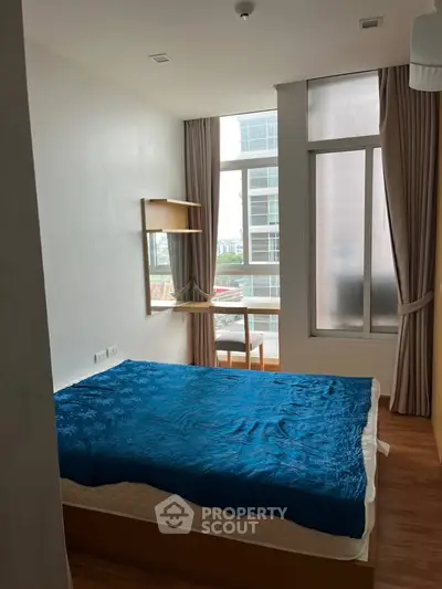 Modern bedroom with large window and blue bedding in a high-rise apartment.