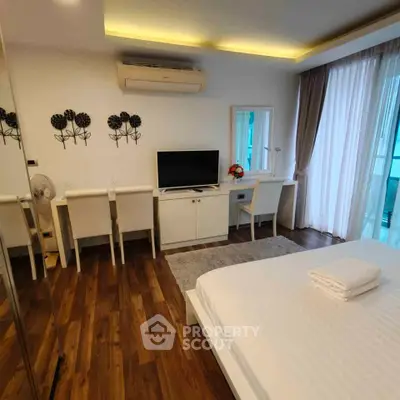 Modern bedroom with wooden flooring, stylish decor, and natural light from large windows.