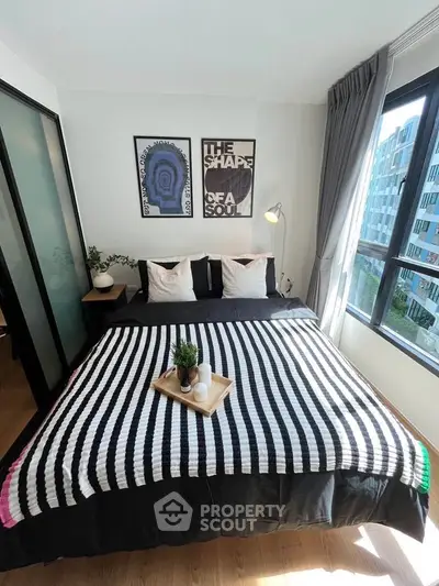 Modern bedroom with stylish decor and large windows offering natural light and city view.