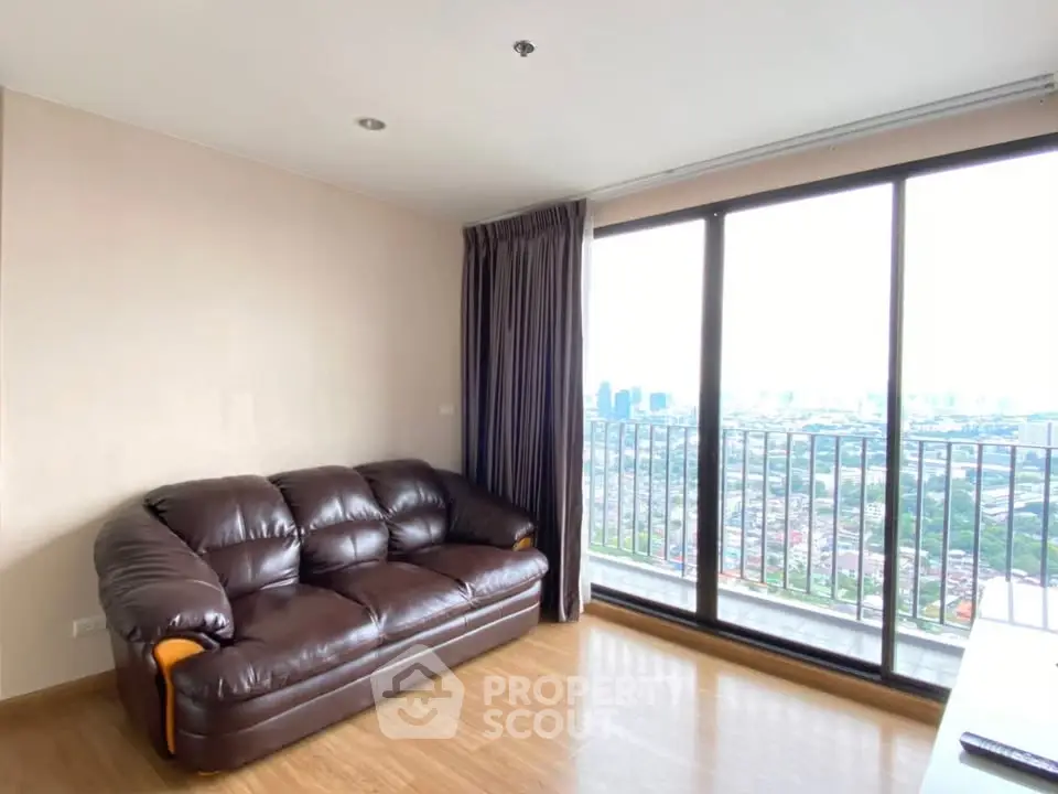 Spacious living room with leather sofa and stunning city view from large windows.