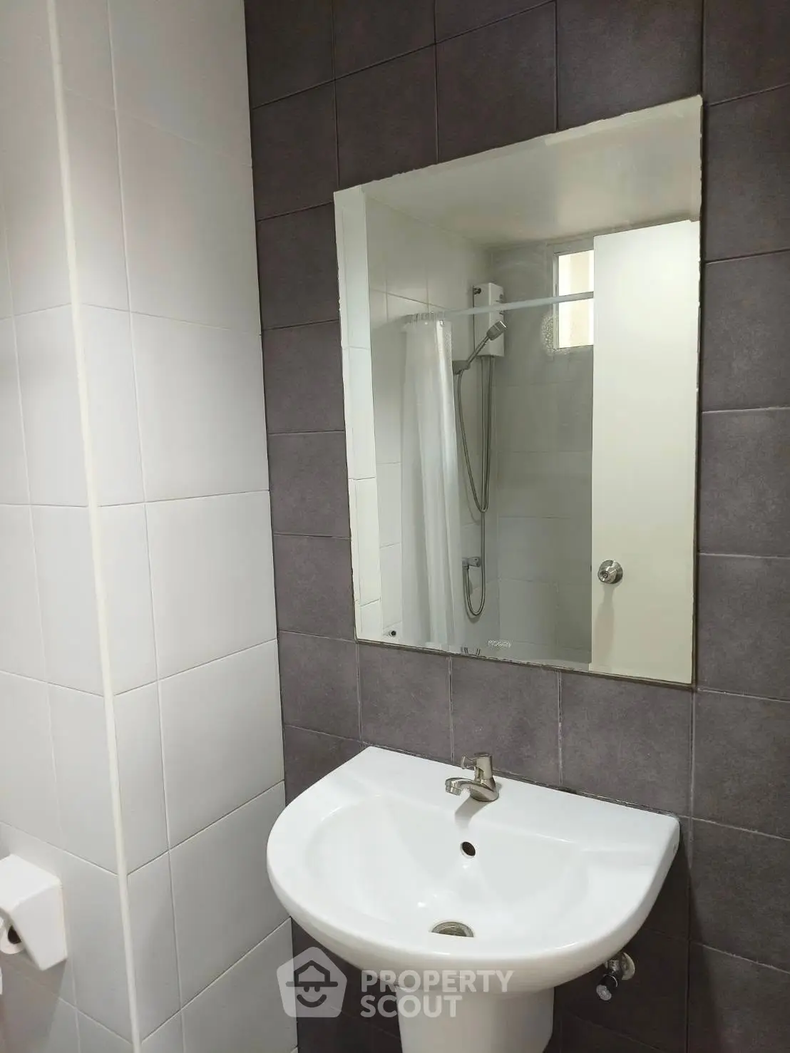 Modern bathroom with sleek sink and mirror, featuring a shower area with neutral tiles.
