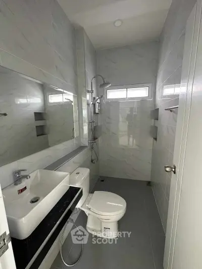 Sleek modern bathroom with glossy marble tiles, wall-mounted sink, and a spacious shower area, illuminated by natural light from frosted windows.
