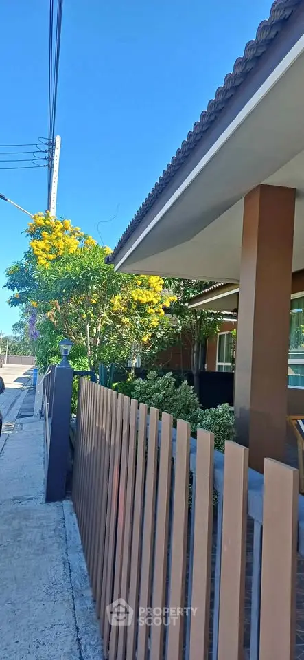 Charming suburban home with lush garden and modern fence under clear blue sky.