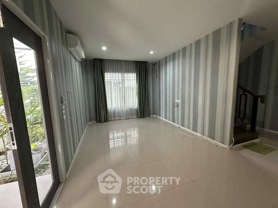 Spacious unfurnished living room with large window and modern striped wallpaper.