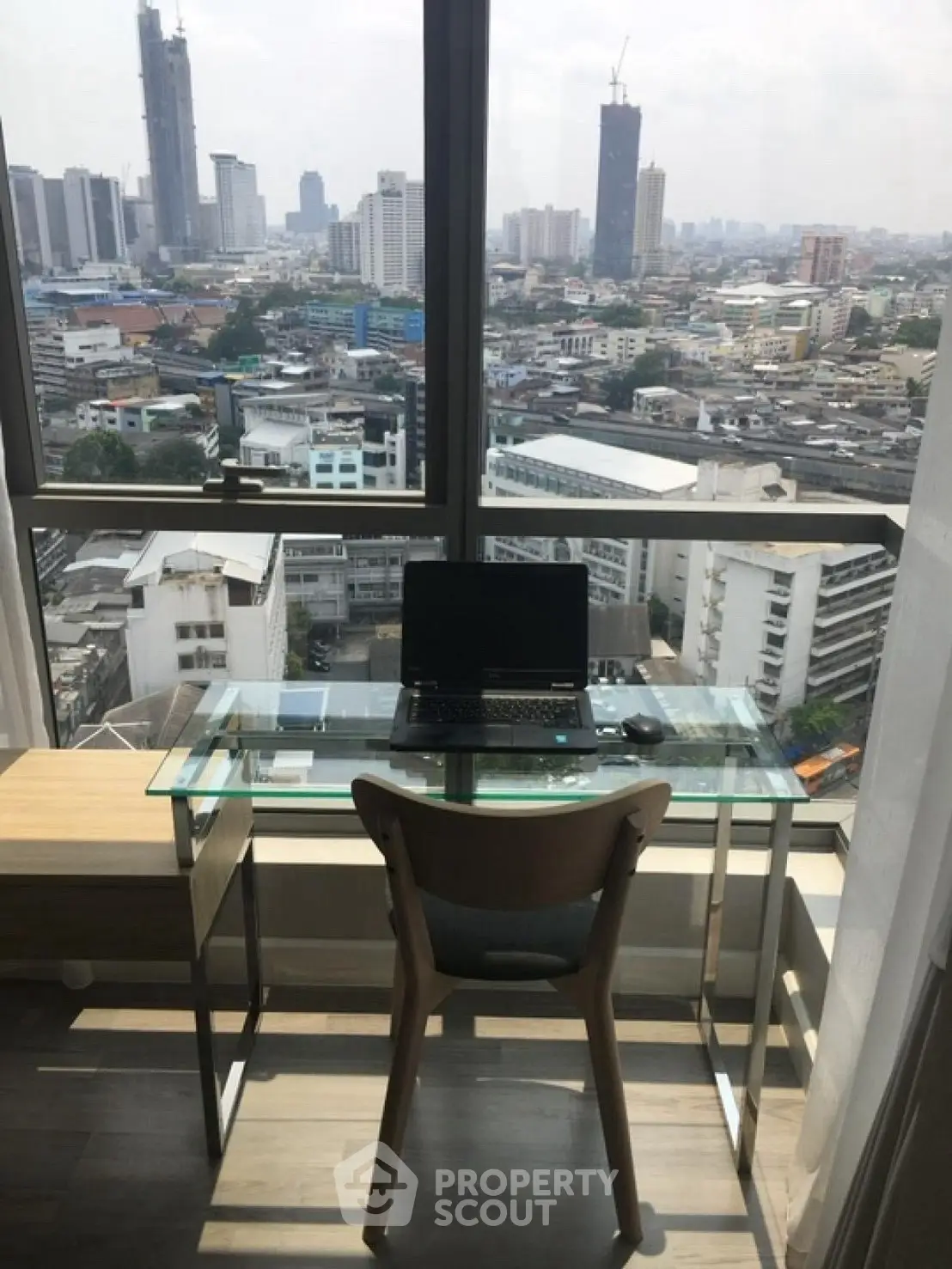 Stunning city view from modern home office with glass desk and laptop.
