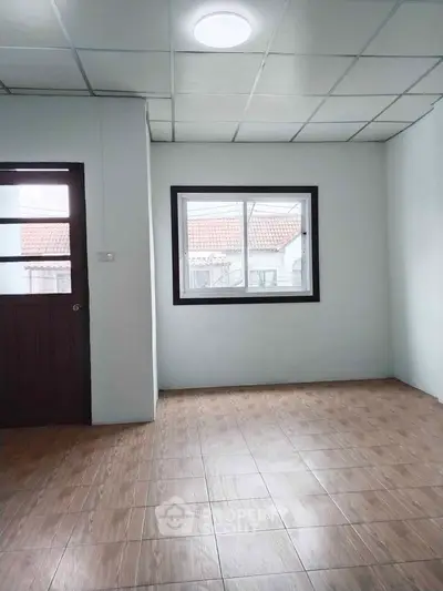 Spacious empty room with wooden flooring and large window, perfect for customization.