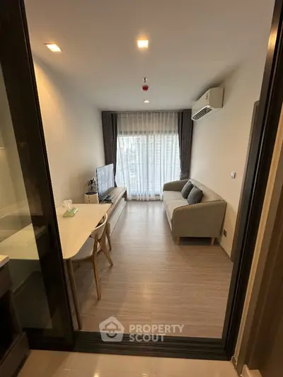 Modern living room with cozy sofa and TV, featuring sleek wooden flooring and natural light.