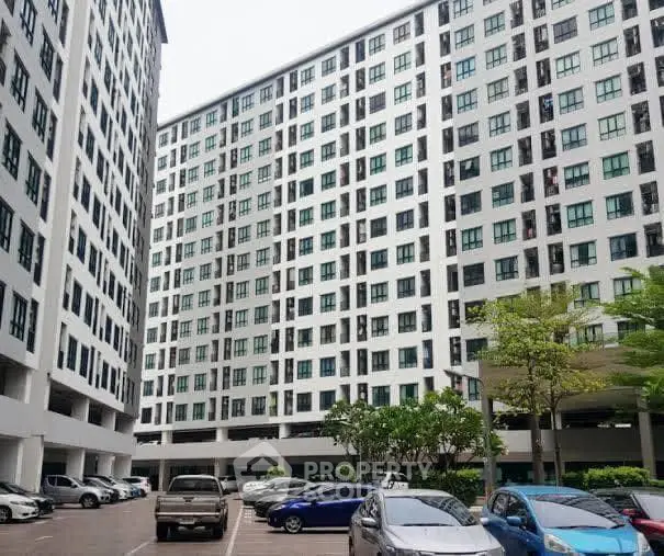 Modern high-rise apartment building with spacious parking area and lush greenery.