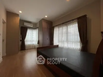 Spacious bedroom with wooden flooring and large windows for natural light.
