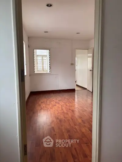 Spacious empty room with wooden flooring and natural light through windows.